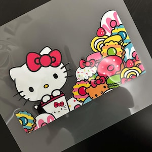 K&ouml;nnte beinhalten: Ein wei&szlig;er Hello Kitty-Charakter mit einer rosa Schleife h&auml;lt eine Tasse Kaffee. Der Hintergrund ist ein farbenfrohes Muster aus Donuts, Streuseln und anderen s&uuml;&szlig;en Leckereien.