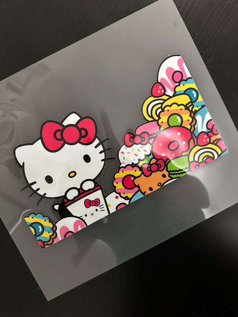 K&ouml;nnte beinhalten: Ein wei&szlig;er Hello Kitty-Charakter mit einer rosa Schleife h&auml;lt eine Tasse Kaffee. Der Hintergrund ist ein farbenfrohes Muster aus Donuts, Streuseln und anderen s&uuml;&szlig;en Leckereien.