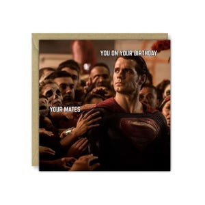 May include: A birthday card featuring a Superman-like figure surrounded by a crowd. The card has the text "YOU ON YOUR BIRTHDAY" at the top and "YOUR MATES" on the left side. The image is set against a brown cardstock background.