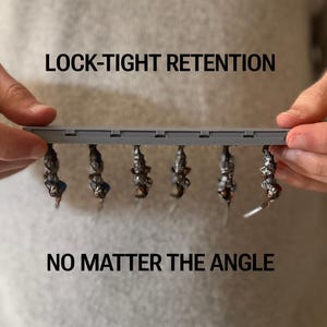 May include: A grey plastic bar with six small, dark objects hanging from it. The text "LOCK-TIGHT RETENTION" and "NO MATTER THE ANGLE" are above and below the bar. The objects appear to be attached securely.