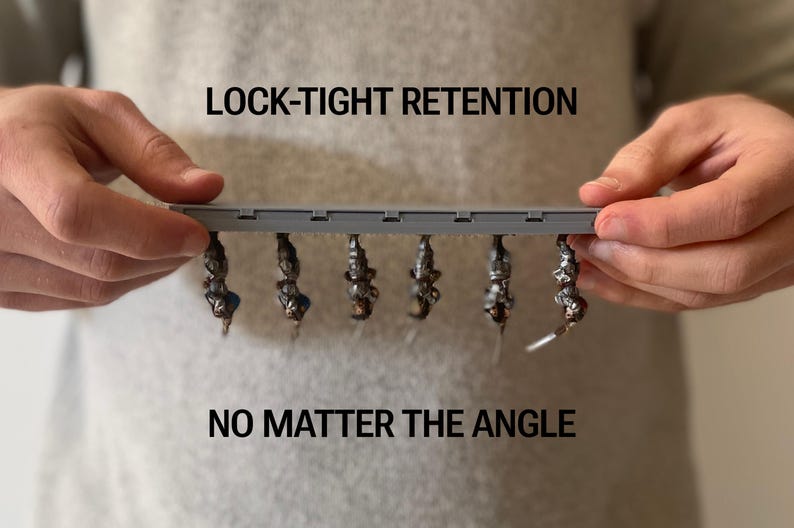 May include: A grey plastic bar with six small, dark objects hanging from it. The text "LOCK-TIGHT RETENTION" and "NO MATTER THE ANGLE" are above and below the bar. The objects appear to be attached securely.