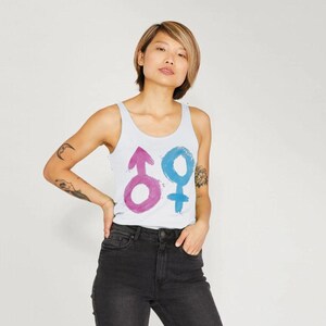 May include: White tank top featuring a pink and blue gender symbol design. The symbols are painted with a watercolor effect. The top is sleeveless and has a scoop neck.