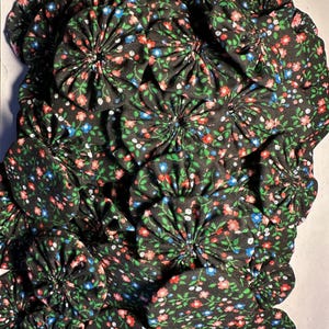 May include: A close-up of a fabric texture with a black background and a floral pattern in shades of pink, blue, and green. The fabric is gathered into a series of circular shapes, creating a three-dimensional effect.