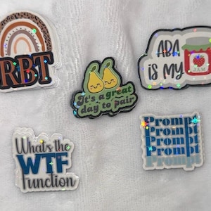 Puede incluir: Una colección de pegatinas holográficas con varios diseños y texto. Una pegatina presenta un arcoíris y las letras "RBT". Otra dice "ABA is my JAM" con un tarro de mermelada. Otras pegatinas dicen "It's a great day to pair", "What's the WTF function" y "Prompt".