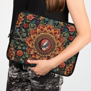 May include: A black laptop sleeve featuring a colorful floral mandala design with orange, red, and green accents. The center of the design includes a Steal Your Face logo. The sleeve is held by a person.