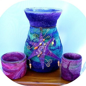 May include: A purple, blue, and green felted vase with a metal starfish design. The vase is surrounded by two smaller purple, blue, and green felted candle holders.