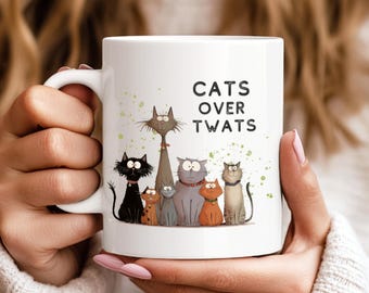 May include: White ceramic coffee mug with a black outline of multiple cats and the text "Cats Over Twats" in black.