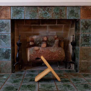 May include: A wooden fireplace tool rests on a tiled floor in front of a fireplace. The fireplace has a brick interior and is framed by green and brown tiles. Two black decorative stands flank the fireplace.