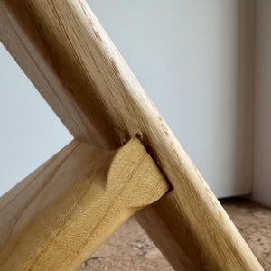 Op de afbeelding: Close-up van een houten meubelverbinding. De lichtbruine houtnerf is zichtbaar. De verbinding is een pen-en-gatverbinding, met een wigvormige pen die in de uitsparing is geplaatst.