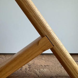 Op de afbeelding: Close-up van een houten meubelverbinding. Twee stukken lichtbruin hout zijn in een hoek verbonden, waarbij het ene stuk in het andere is gestoken. De houtnerf is zichtbaar en de verbinding is precies.