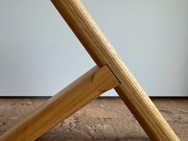Op de afbeelding: Close-up van een houten meubelverbinding. Twee stukken lichtbruin hout zijn in een hoek verbonden, waarbij het ene stuk in het andere is gestoken. De houtnerf is zichtbaar en de verbinding is precies.