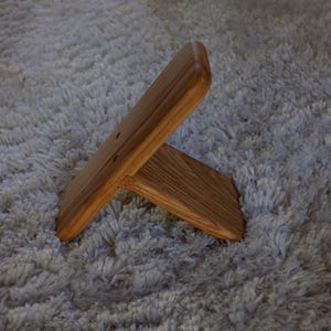 Op de afbeelding: Een houten standaard met een natuurlijke afwerking. De standaard is gemaakt van twee stukken hout die in een rechte hoek zijn verbonden, waardoor een stabiele basis ontstaat. De houtnerf is zichtbaar. De standaard is ontworpen om een klein object vast te houden.