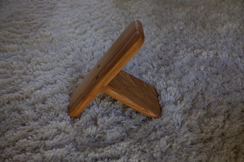 Op de afbeelding: Een houten standaard met een natuurlijke afwerking. De standaard is gemaakt van twee stukken hout die in een rechte hoek zijn verbonden, waardoor een stabiele basis ontstaat. De houtnerf is zichtbaar. De standaard is ontworpen om een klein object vast te houden.
