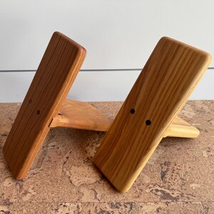 May include: Two angled wooden stands with a natural light brown wood grain finish. Each stand features a rectangular front panel with two small, dark circular holes positioned horizontally near the center, supported by a triangular base piece.