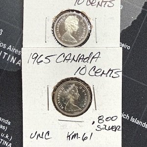 Könnte beinhalten: Zwei kanadische 10-Cent-Münzen von 1965, jeweils in einem Kartonhalter. Die Münzen zeigen das Profil von Königin Elisabeth II. Auf den Haltern steht "1965 CANADA 10 CENTS" und "UNC KM-61". Ein Halter ist mit ".800 Silver" markiert.