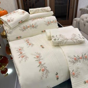 Può includere: Set di biancheria da letto color crema con motivi floreali ricamati in pesca e verde. Il set include un lenzuolo piano, un lenzuolo con angoli, federe e un cuscino decorativo. Il ricamo aggiunge un tocco di eleganza all'arredamento della camera da letto.