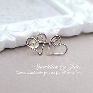 May include: A pair of silver heart-shaped earrings with a swirl design. The earrings are handmade and are a unique piece of jewelry.