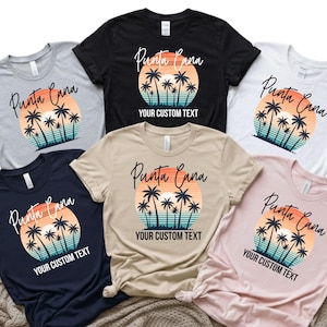 May include: A collection of t-shirts in various colors, including gray, black, white, navy, tan, and pink. Each shirt features a sunset design with palm trees and the words "Punta Cana" and "YOUR CUSTOM TEXT".