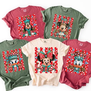 May include: Five short-sleeved crew neck t-shirts in red, olive green, and cream. Each shirt features a graphic of a Disney character dressed as a nutcracker or in festive attire, set against a background of red and white polka-dot stripes.