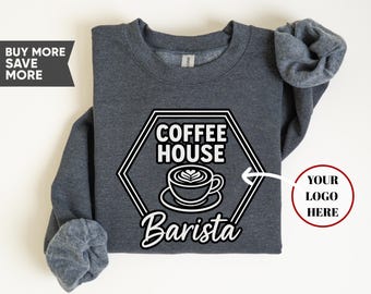May include: A dark gray sweatshirt with a white and black graphic. The graphic features the words "COFFEE HOUSE" and "Barista" around a coffee cup design. The sweatshirt has a crew neck and long sleeves.