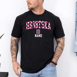 May include: A black short-sleeved t-shirt featuring the text HRVATSKA in a red and white checkered pattern, with the number 10 and the word NAME printed in white below the text in a bold, block-style font centered on the chest area.