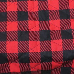 May include: Close-up of a quilted fabric with a classic red and black buffalo check pattern. The fabric is divided into large squares, creating a bold and timeless design. The stitching adds texture and dimension to the material.