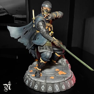 Può includere: Statuetta dettagliata di un guerriero samurai in posa dinamica, con una katana verde. La figura indossa un abito blu e nero con un mantello strappato, una maschera e una fascia. La base è grigia con accenti di foglie arancioni.
