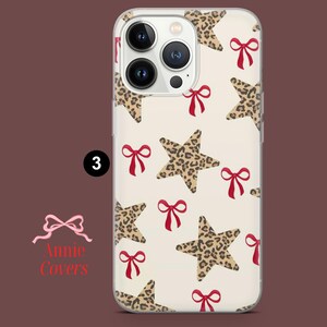 Puede incluir: Funda transparente para tel&eacute;fono con un estampado de estrellas con estampado de leopardo y lazos rojos sobre un fondo crema. La funda tiene un borde transparente y un recorte para la c&aacute;mara. El n&uacute;mero "3" es visible.