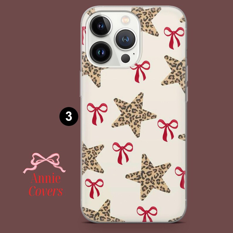 Puede incluir: Funda transparente para tel&eacute;fono con un estampado de estrellas con estampado de leopardo y lazos rojos sobre un fondo crema. La funda tiene un borde transparente y un recorte para la c&aacute;mara. El n&uacute;mero "3" es visible.