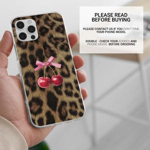 Puede incluir: Funda transparente para tel&eacute;fono con estampado de leopardo y un par de cerezas rojas atadas con un lazo rosa. La funda tiene un recorte para c&aacute;mara de tres lentes. El texto en la imagen dice "PLEASE READ BEFORE BUYING".