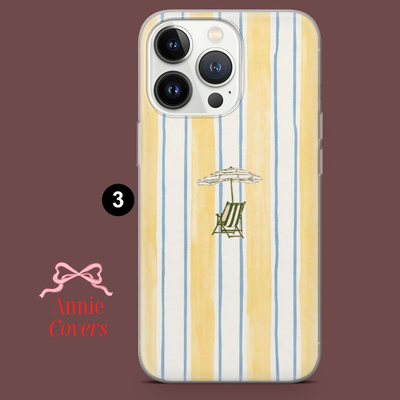 May include: A clear phone case with a yellow and blue striped pattern. The case features a small illustration of a beach umbrella and a chair. The number "3" is printed on the case. The text "Annie Covers" is also printed on the case.