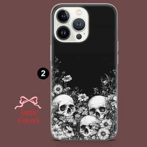 Puede incluir: Carcasa de tel&eacute;fono negra y blanca con un dise&ntilde;o de tres calaveras rodeadas de flores. La carcasa es transparente y tiene un fondo negro.