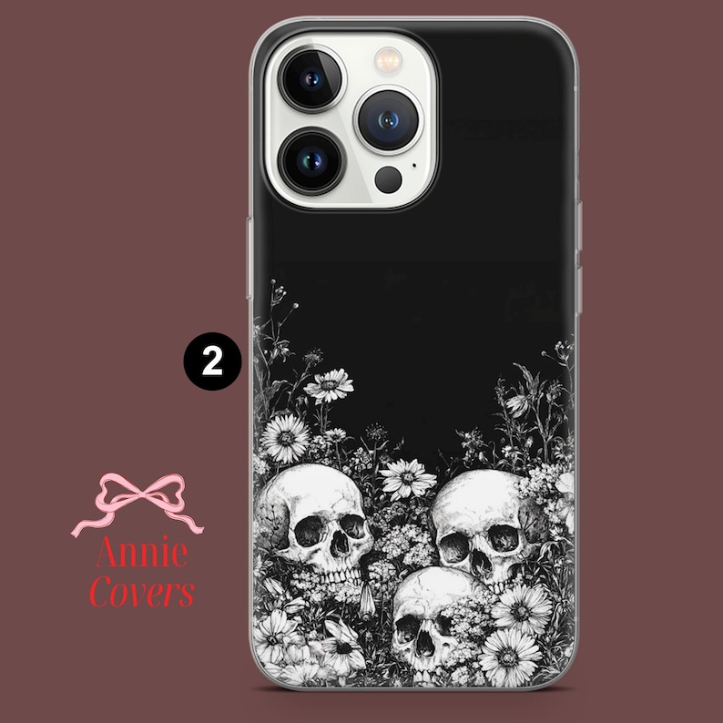 Puede incluir: Carcasa de tel&eacute;fono negra y blanca con un dise&ntilde;o de tres calaveras rodeadas de flores. La carcasa es transparente y tiene un fondo negro.