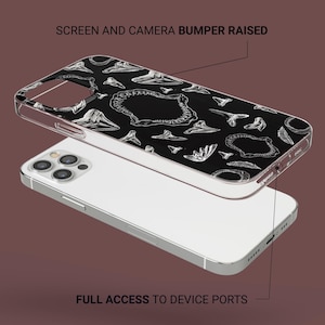 Pode incluir: Uma capa transparente para telefone com uma estampa em preto e branco de dentes e mand&iacute;bulas de dinossauro. A capa tem um para-choque elevado para proteger a tela e a c&acirc;mera. "SCREEN AND CAMERA BUMPER RAISED" e "FULL ACCESS TO DEVICE PORTS" est&atilde;o escritos na imagem.
