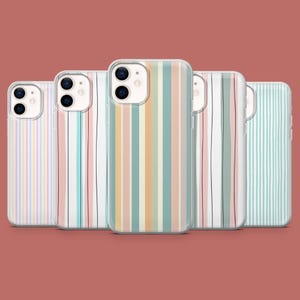 May include: Five clear phone cases with colorful vertical stripe designs. The stripes include pastel shades of pink, blue, yellow, and green, with some cases featuring thin black lines. The cases are arranged in a row against a solid red-brown background.