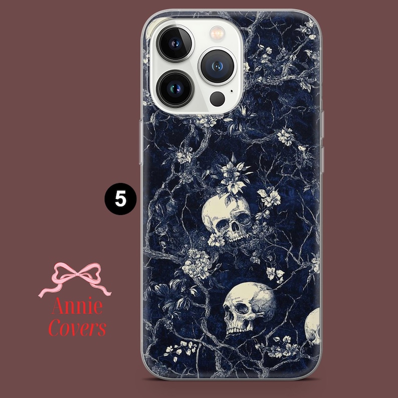 Puede incluir: Una funda transparente para tel&eacute;fono con un patr&oacute;n floral azul oscuro y blanco con calaveras. La funda tiene una protuberancia de c&aacute;mara elevada con un borde blanco.
