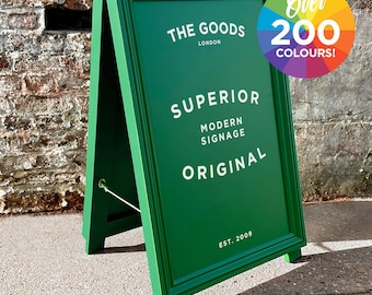 Könnte beinhalten: Ein grünes A-förmiges Schild mit dem Text "THE GOODS LONDON" und "SUPERIOR MODERN SIGNAGE ORIGINAL EST. 2009". Das Schild steht auf einem Bürgersteig vor einer Backsteinmauer.
