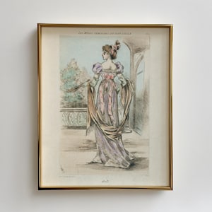 Puede incluir: Una impresión enmarcada de una mujer con un vestido morado y rosa con una chal marrón. La impresión está titulada "Les Modes Féminines du Salon de Paris" y fechada en 1865.