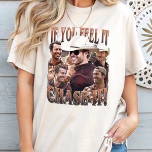 May include: A white t-shirt with a graphic print of five men wearing cowboy hats and the text "If you feel it chase it!"