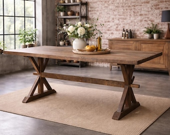 May include: A large, rectangular wooden dining table with a trestle base. The table is made of dark brown wood and sits on a beige rug. A white vase with flowers and a wooden tray with fruit are on the table. A wooden cabinet and brick wall are in the background.