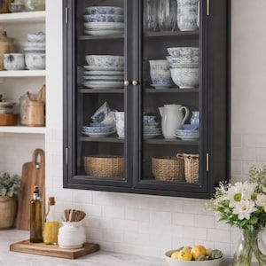 May include: A black cabinet with glass doors displays blue and white patterned crockery, bowls, and a teapot. Woven baskets sit at the bottom. The cabinet is mounted on a white tiled wall above a marble countertop.