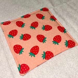 Peut inclure: Un dessous de verre carré en tissu avec un motif répété de fraises rouges et de tiges vertes sur un fond rose clair à pois blancs. Le dessous de verre a une bordure cousue.