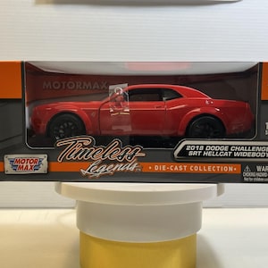 May include: A red 2018 Dodge Challenger SRT Hellcat Widebody die-cast model car in its original packaging. The box features the MotorMax logo, Timeless Legends branding, and a 1:24 scale indicator. The packaging includes safety warnings.