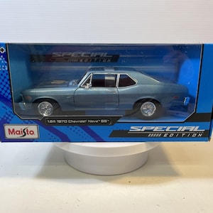 May include: A 1:24 scale die-cast 1970 Chevrolet Nova SS model car in metallic blue, displayed inside a blue Maisto Special Edition box. The packaging features clear plastic windows, the Maisto logo, and text identifying the vehicle model.