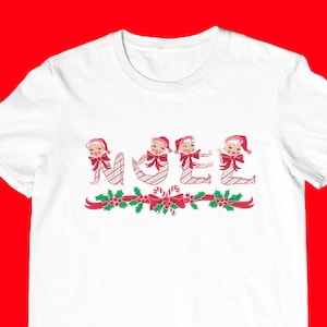 Puede incluir: Camiseta blanca con un diseño navideño rojo y verde con la palabra "NOEL" escrita con duendes de dibujos animados.