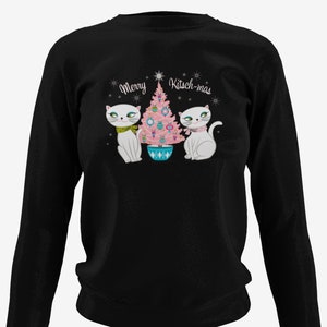 Puede incluir: Sudadera negra de manga larga con un árbol de Navidad rosa, dos gatos blancos y el texto "Merry Kitsch-mas".