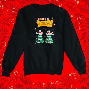 Puede incluir: Sudadera negra con un diseño navideño retro. El gráfico presenta dos árboles de Navidad con figuras de Papá Noel y el texto "Merry Christmas and Happy New Year" en una pancarta.