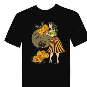 May include: A black t-shirt with a graphic of a woman in a green and yellow dress holding a jack-o'-lantern. The background features a moon, a castle, and bats. There are also several pumpkins in the foreground.