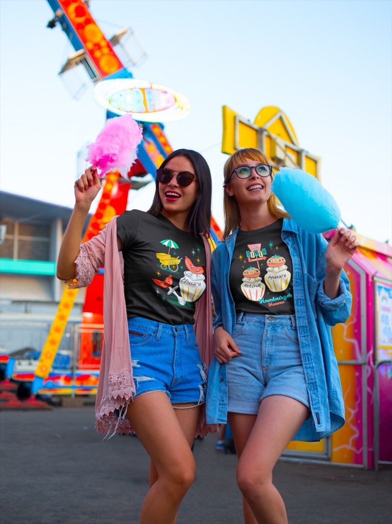May include: Two friends wearing black t-shirts with colorful graphic prints. The t-shirts feature illustrations of jars with the text "Sugar & Spice" and "Everything Nice". The friends are holding pink and blue cotton candy.