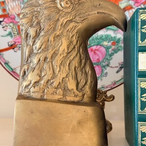 May include: A brass eagle head bookend. The bookend is a detailed sculpture of an eagle's head and beak, with textured feathers. The base is rectangular. The bookend is a decorative item for home decor.